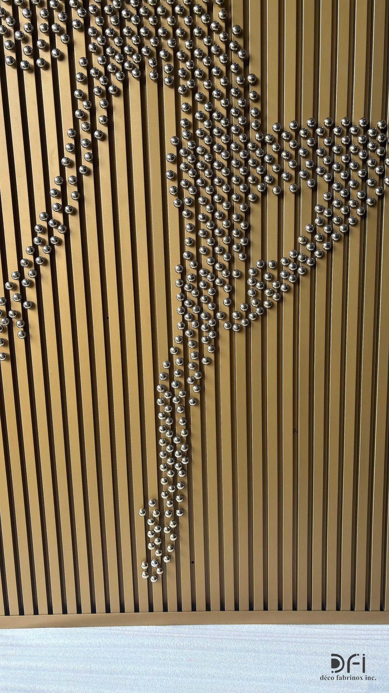 Dancing figure in steel spheres on a fluted gold metal panel
