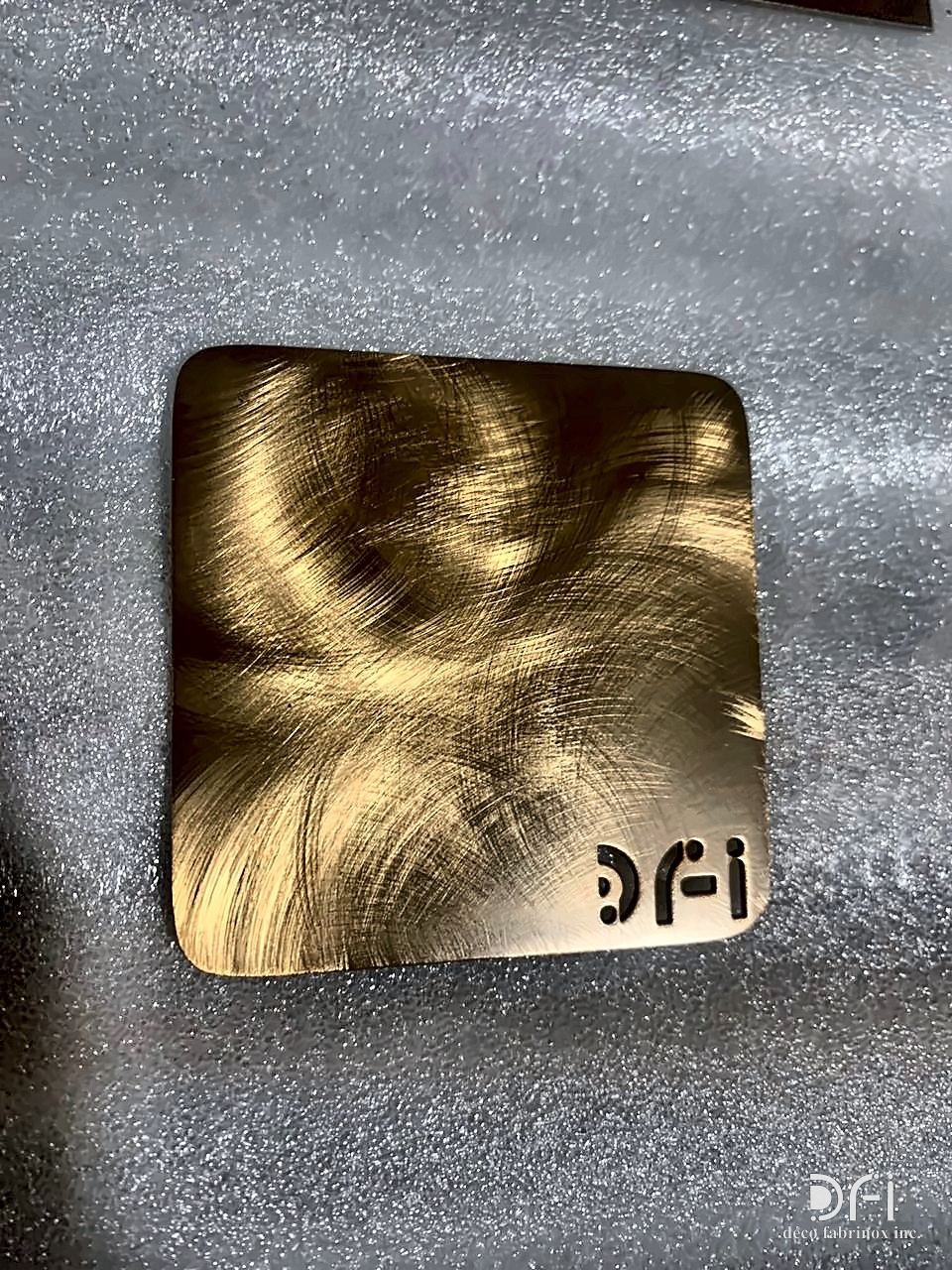 Swirl-brushed brass sample with the DFI mark cut in